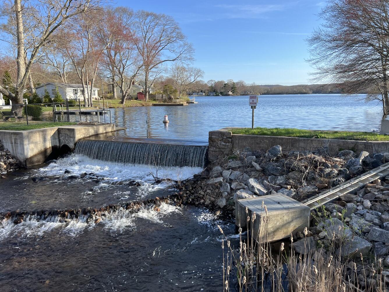 water flowing over a dam and the fish ladder with rocks, trees and homes in the background, blue sky in Old Lyme, Connecticut