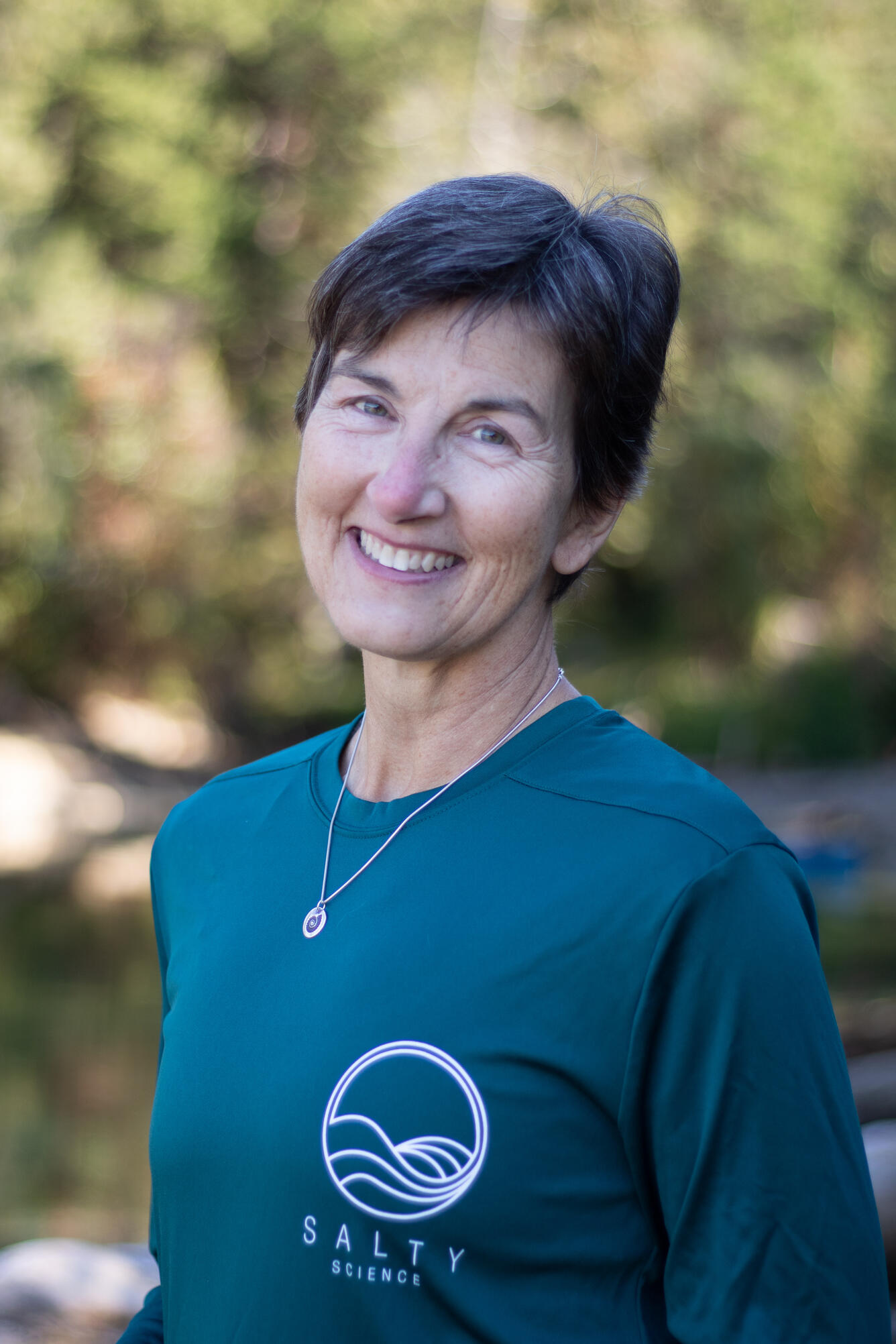 A woman with short hair, glasses and a green shirt smiles for her picture.