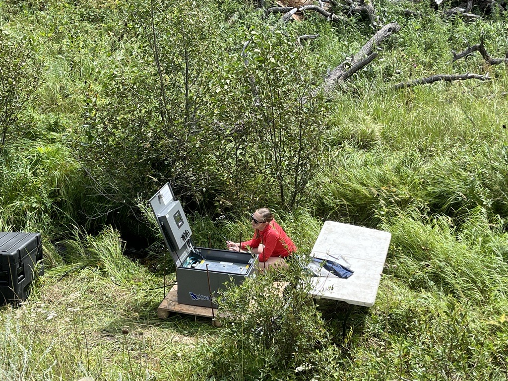 eDNA autosampler next to creek with researcher kneeling next to it