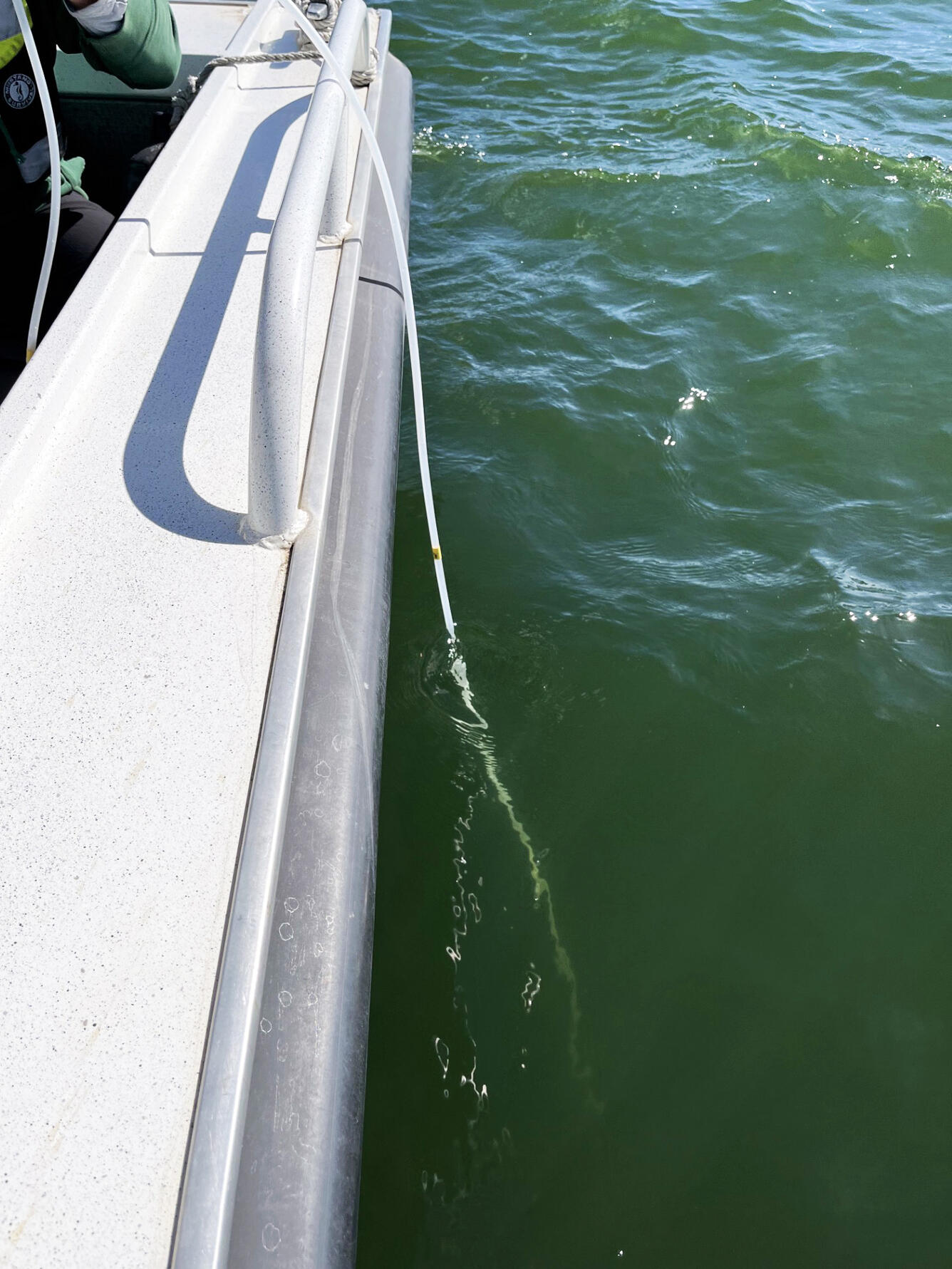 From a boat, an eDNA sampler connected to a hose is lowered into a reservoir to identify invasive aquatic species
