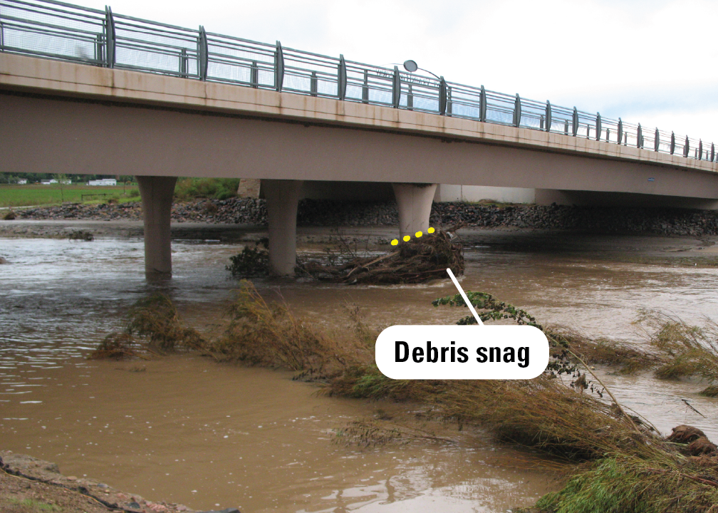 A pile of branches and vegetation has caught on a pier underneath a highway bridge over a river.