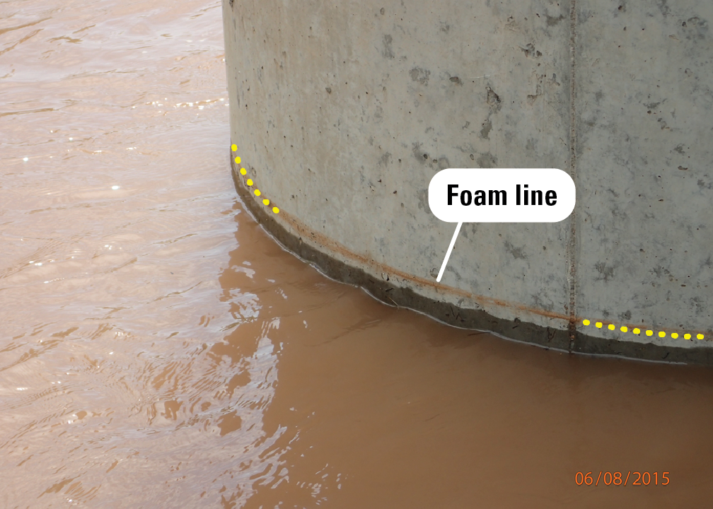A dry, rust-colored foam line encircles a bridge pier a few inches above the current water surface.