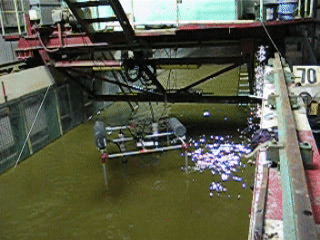 A moving photo shows a metal frame moving slowly back and forth in a narrow water way with murky water.