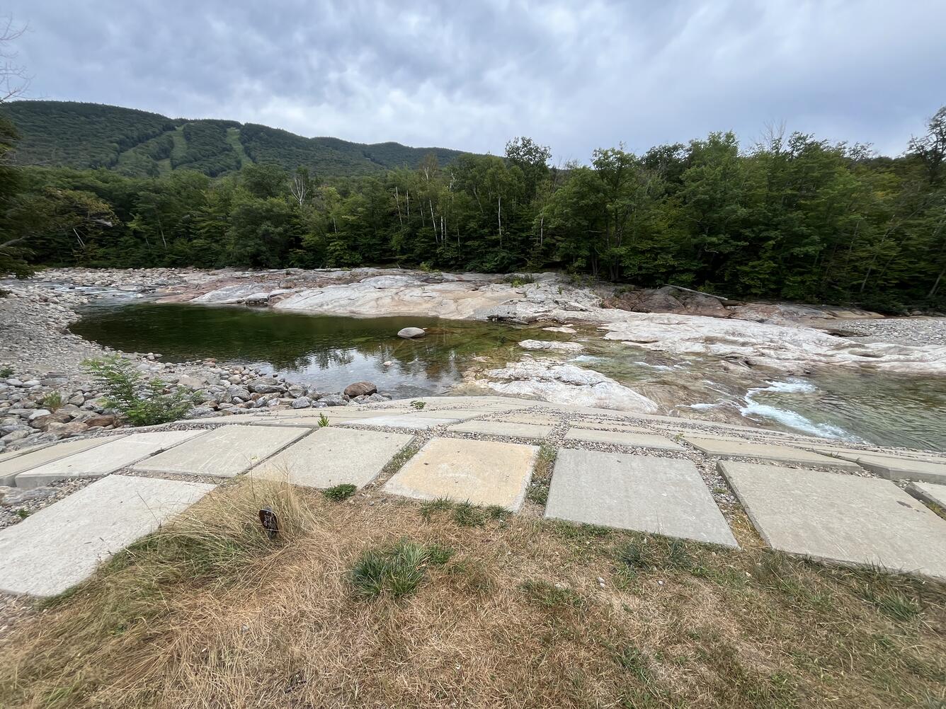 Low lying water in a river with a ski resort in the background during the summer.