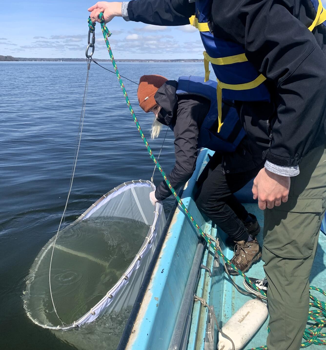 Scientist collects plankton in water by holding a large net over the side of a boat