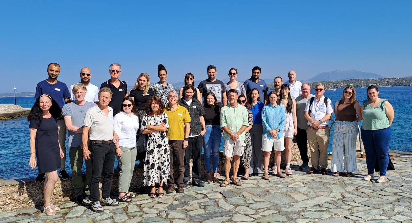 This is a group of people standing in front of the Mediterranean Sea in Spetses Island, Greece. 