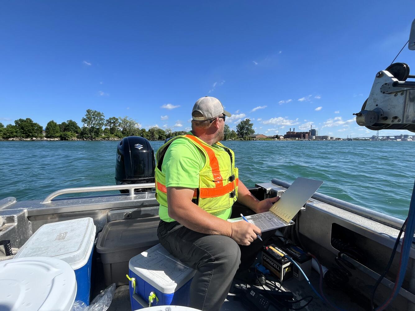 Hydrologic technician on a boat, holding a laptop looks over a blue river