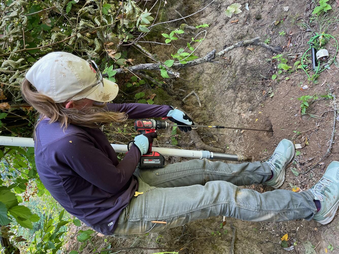 male hydrologist drills down into brown soil to create an opening for the piezometer