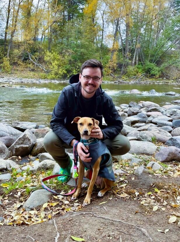 Photo of Joseph Zemmels, a data scientist as USGS. In the background is a flowing river, bed rocks, and fall trees.