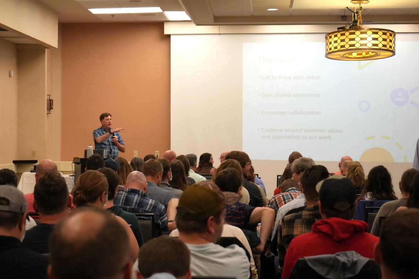 Man standing at podium speaking into a microphone to a large group of people