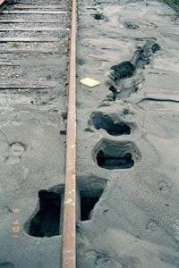 Photo of sand being ejected through cracks, forming holes along railroad tracks