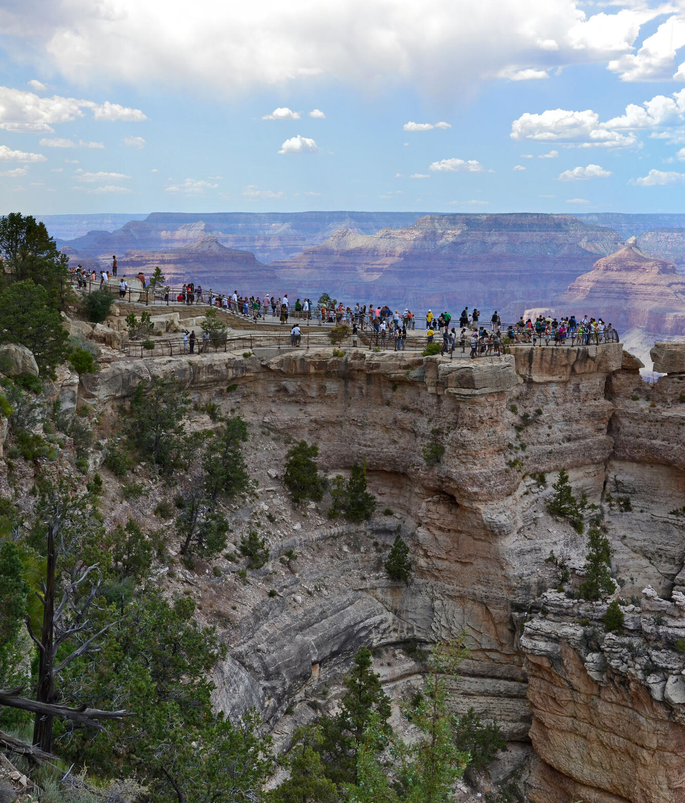 a crowd of people in the distance stand on top of a large viewing platform in the grand canyon