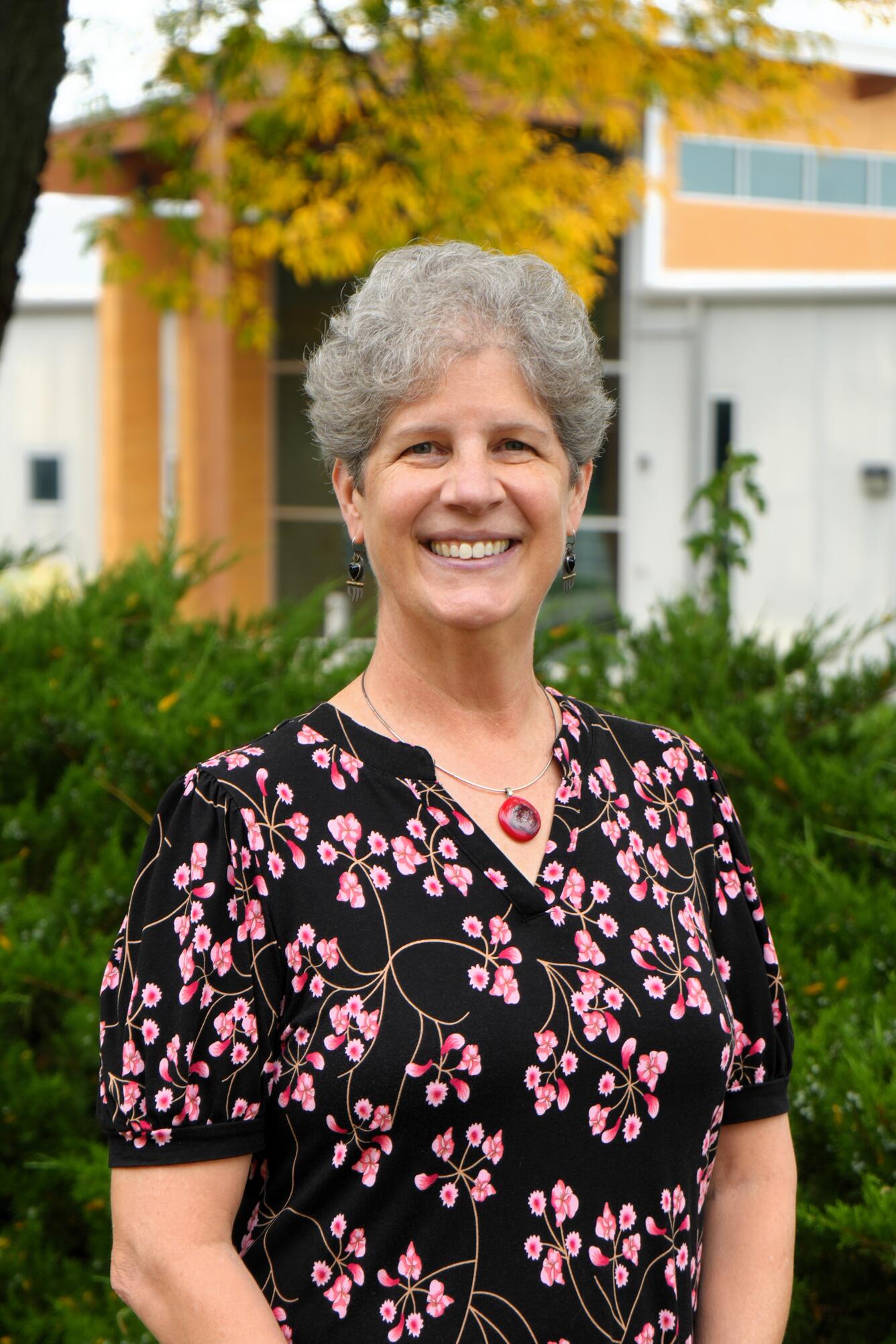 Woman smiling against backdrop of building and tree with yellow leaves