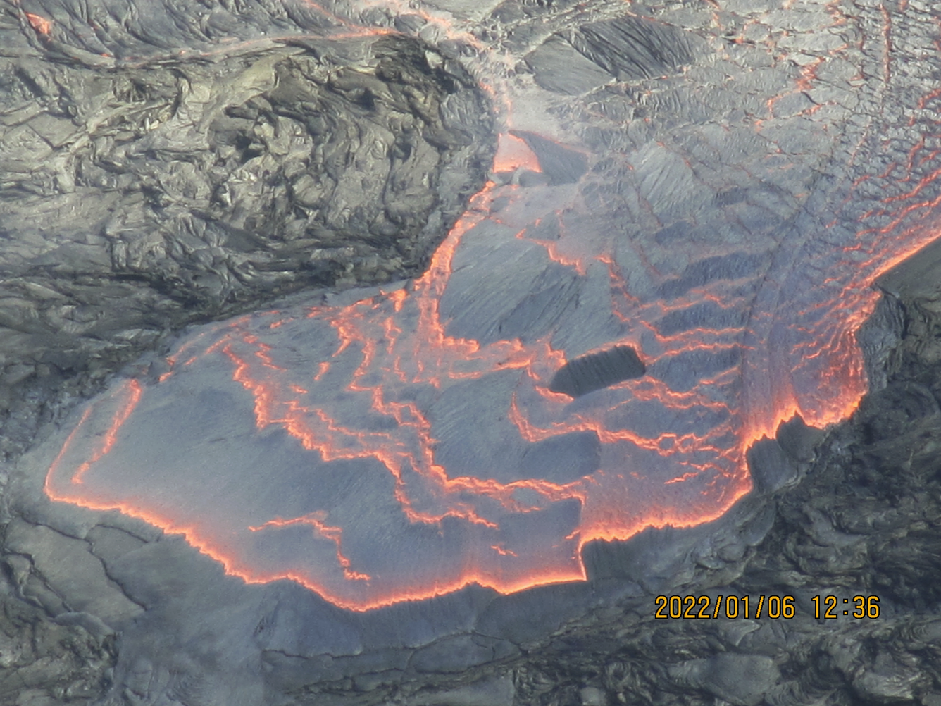 Color photograph showing a close-up view of a lava lake with gray surface crust