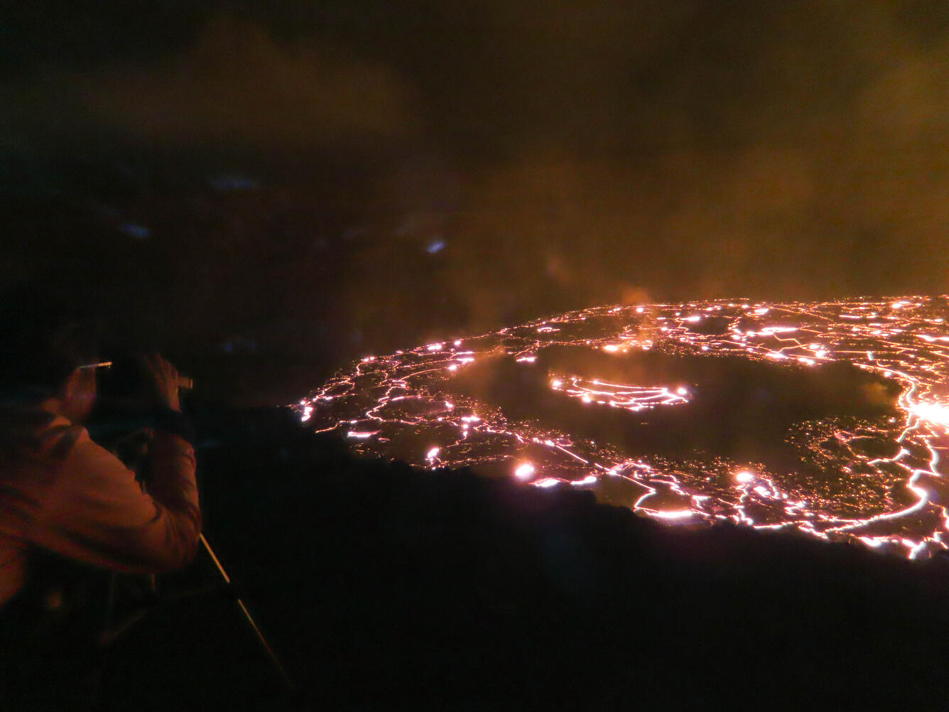 person looking through scope toward orange glow of lava lake with a black background