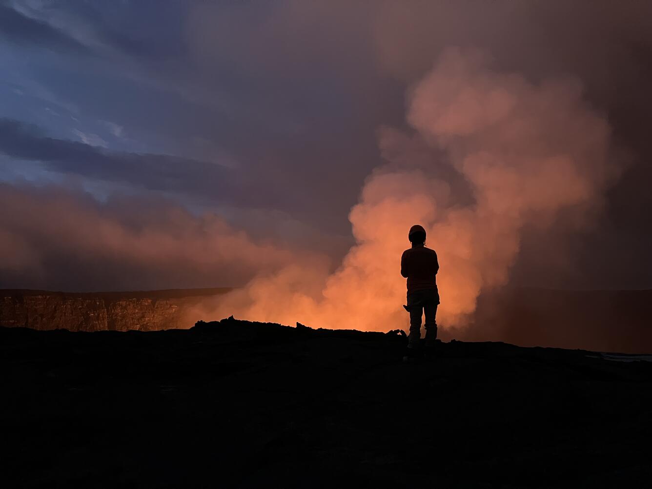 Color photograph of scientist outline against eruption glow
