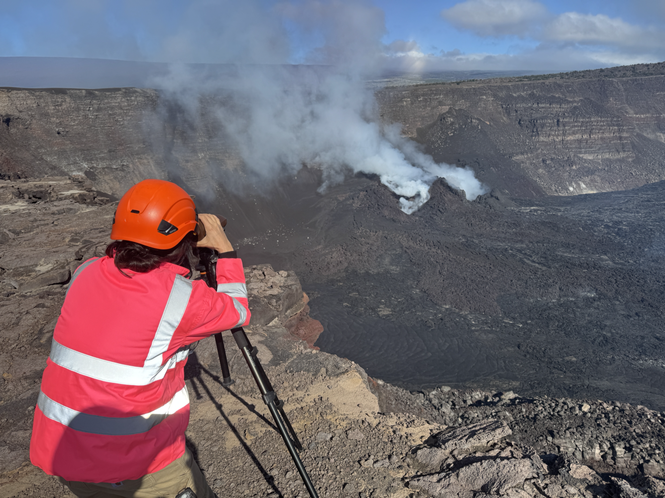 Scientist looks through a laser rangefinder at steaming vents within a crater to make measurements