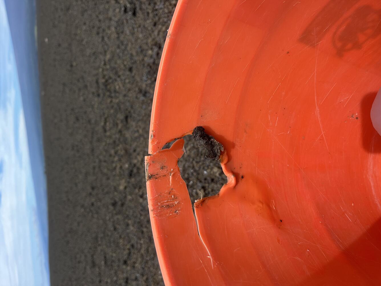 Color photograph of rock stuck in melted edge of plastic bucket