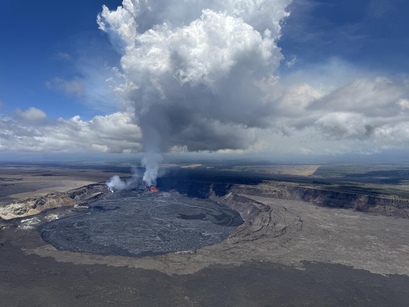 A large white and blue plume rises from the red lava fountains within a crater