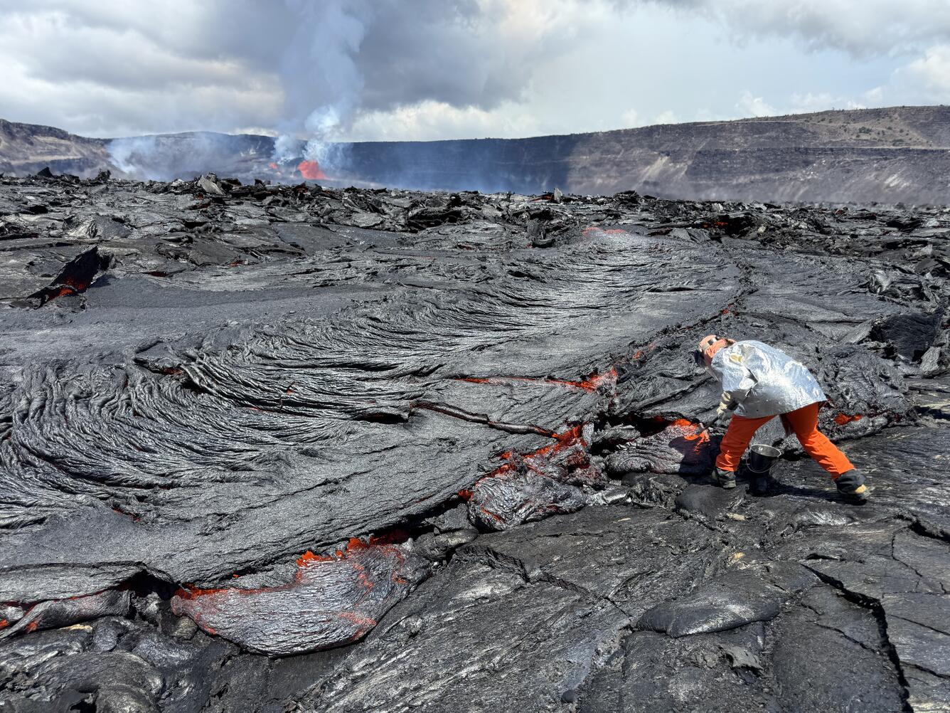 Scientist uses a hammer to collect a red molten lava sample from a lava flow.