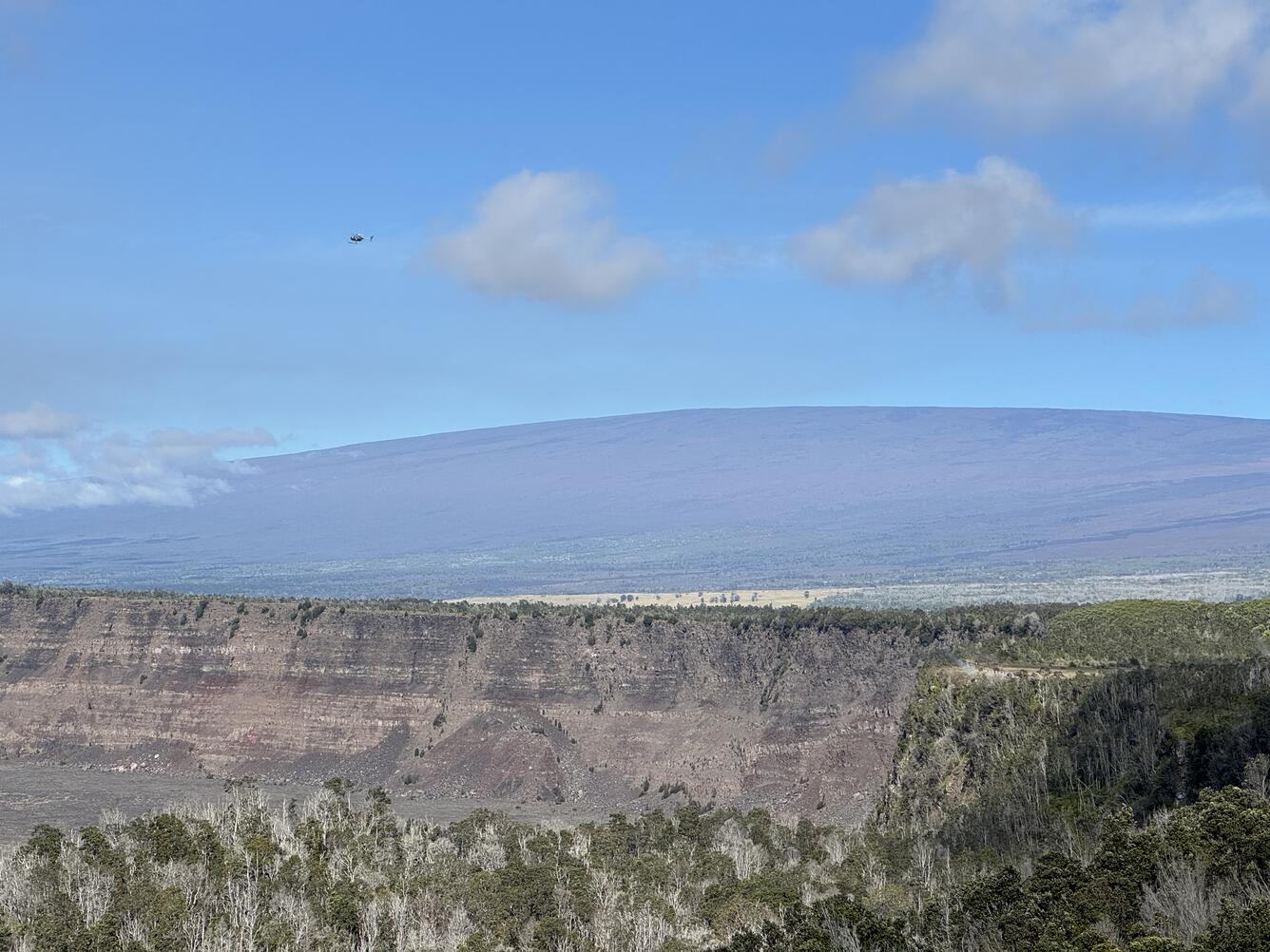 Color photograph of shield volcano with caldera wall in the foreground