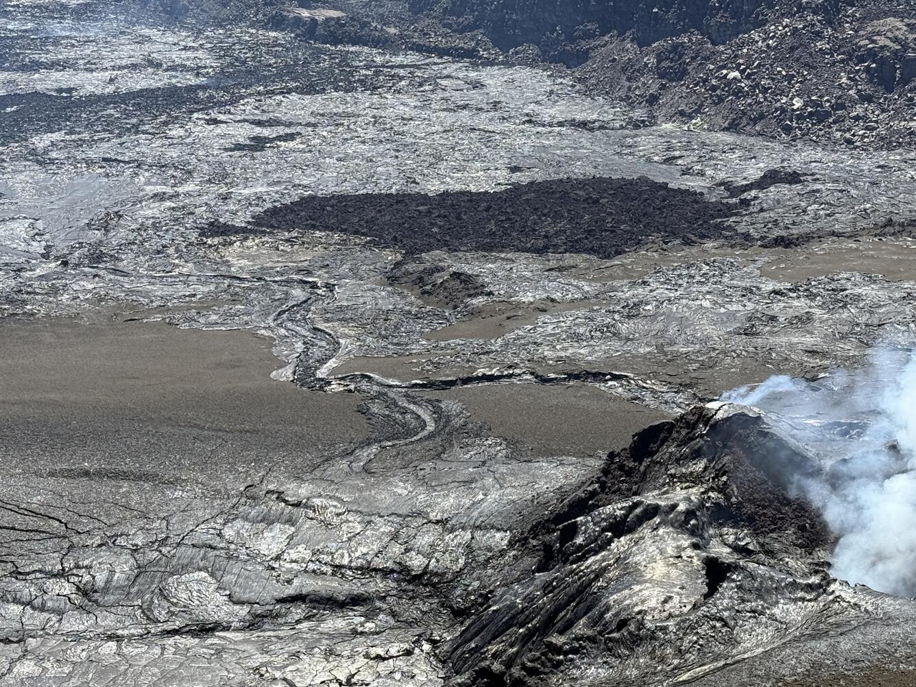 Color photograph of volcanic vent degassing, with recent lava flows and tephra material nearby