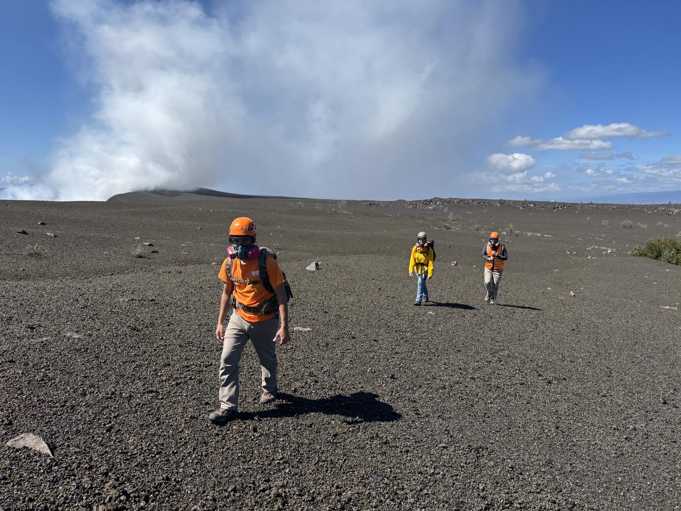 Color photograph of scientists walking across a new geologic deposit wearing safety gear