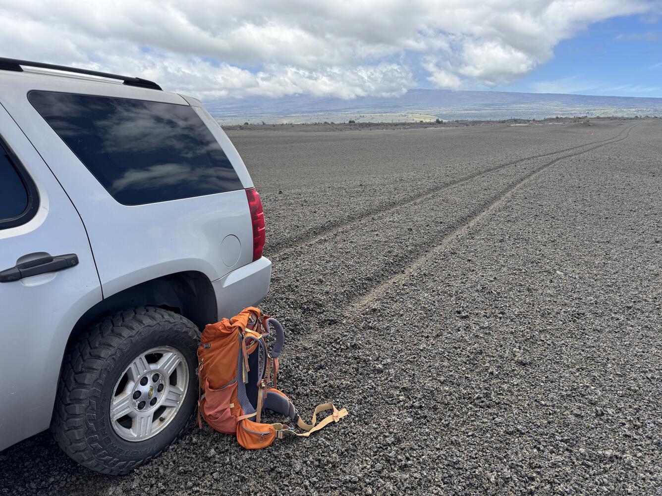 Color photograph of vehicle on volcanic terrain with tire tracks in the background