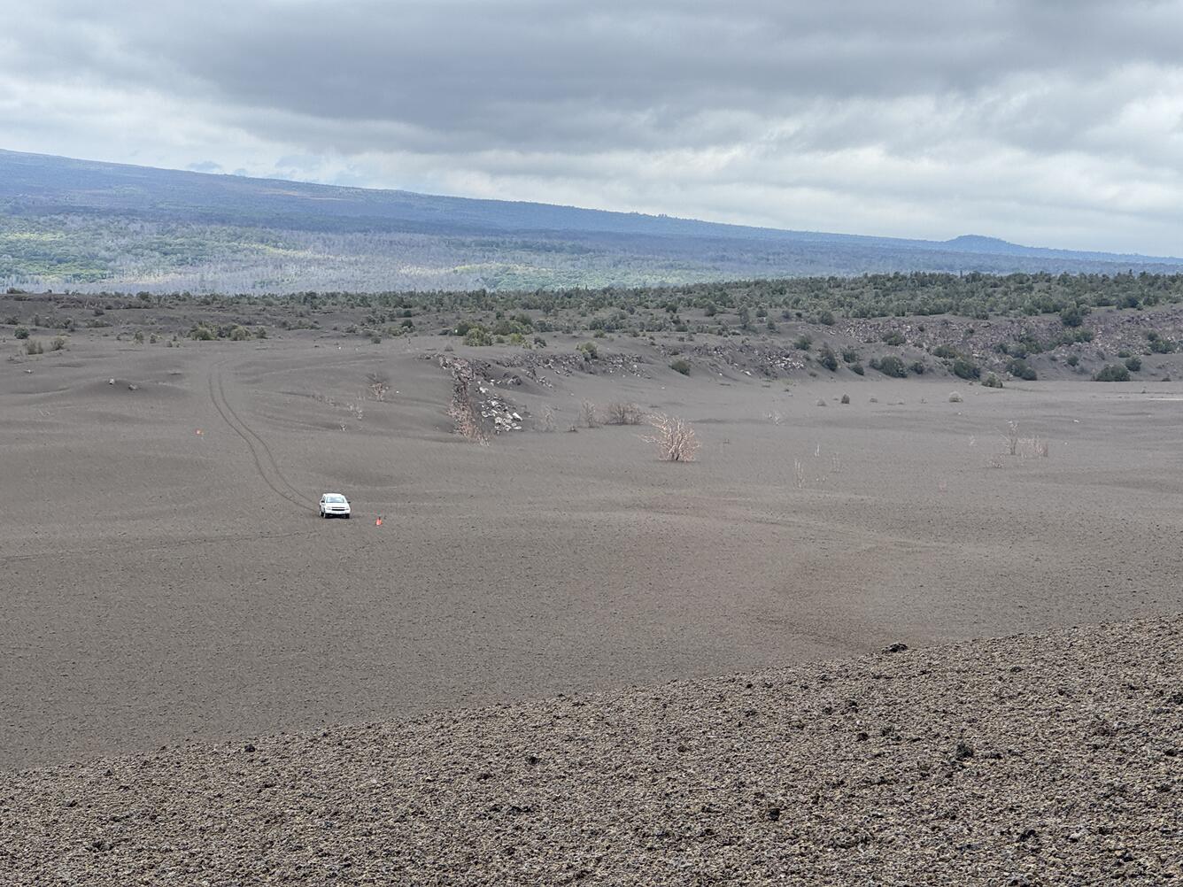Color photograph of volcanic landscape with car driving in the distance