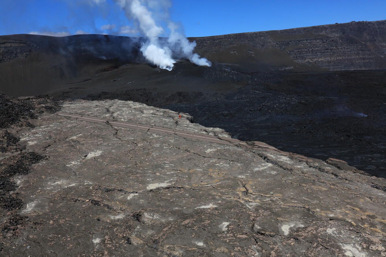 color photo of a scientists working on a field site from a distance with the vents in the background. 