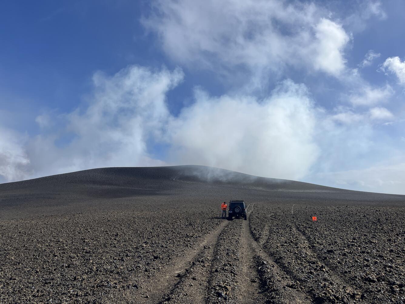 Color photograph of volcanic hill with road and vehicle in the foreground
