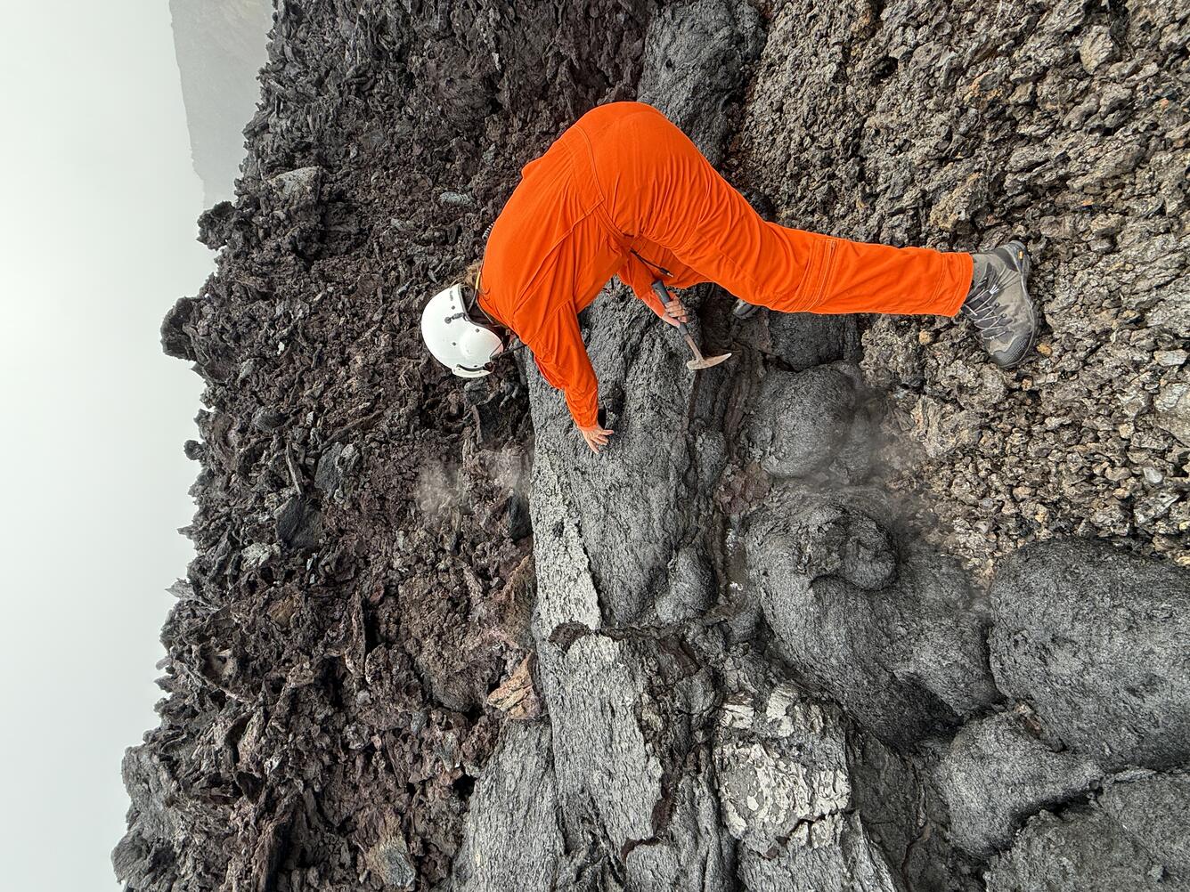 Color photograph of scientist collecting sample of cooled lava flow