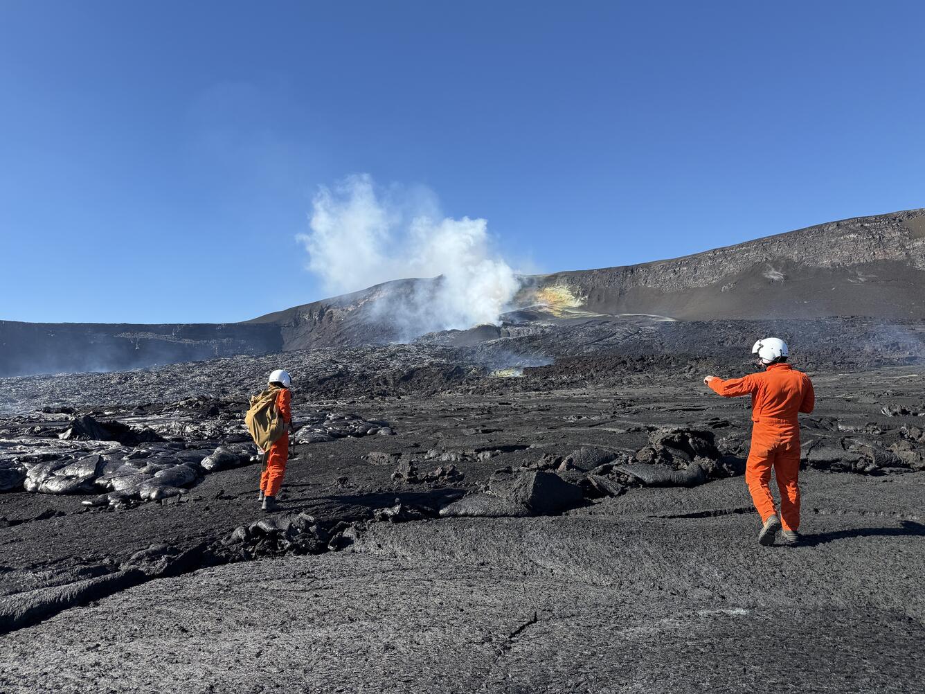 Color photograph of scientists in orange flight suits on a volcanic landscape