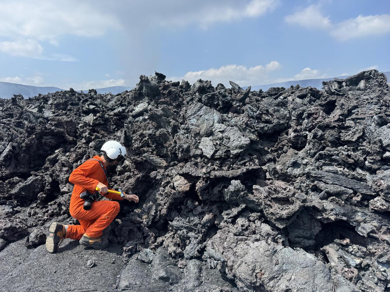 Color photograph of scientist collecting sample of lava flow