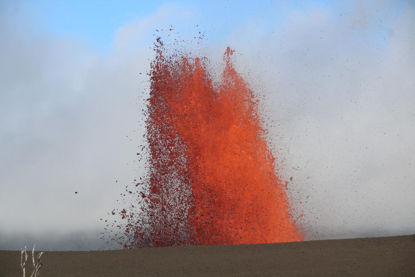 Color photograph of lava fountain visible above crater rim