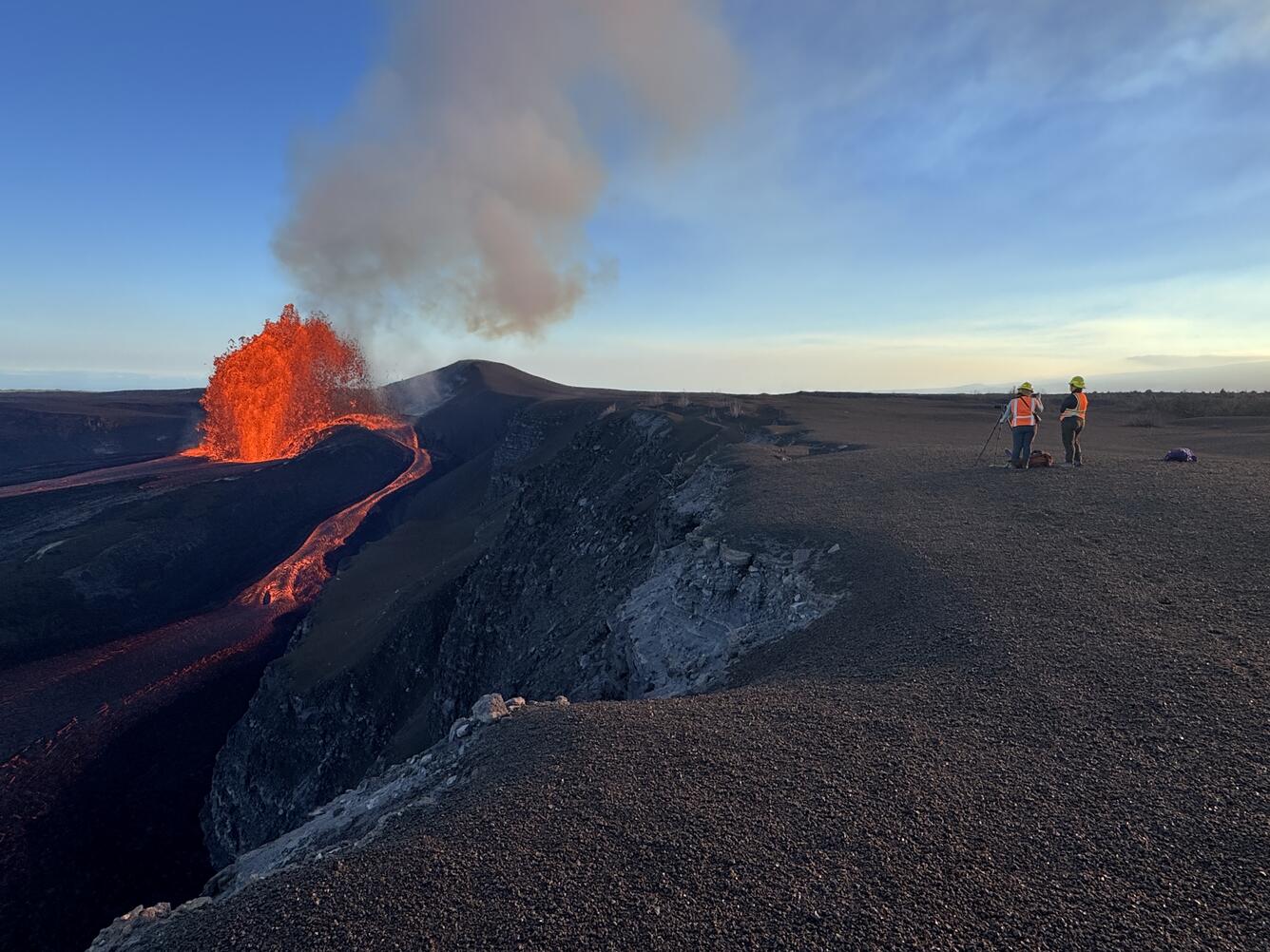 Color photograph of geologists on volcanic crater rim watching lava fountain