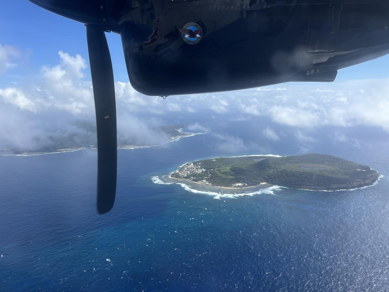 Color photograph of island with part of airplane visible in top of photo