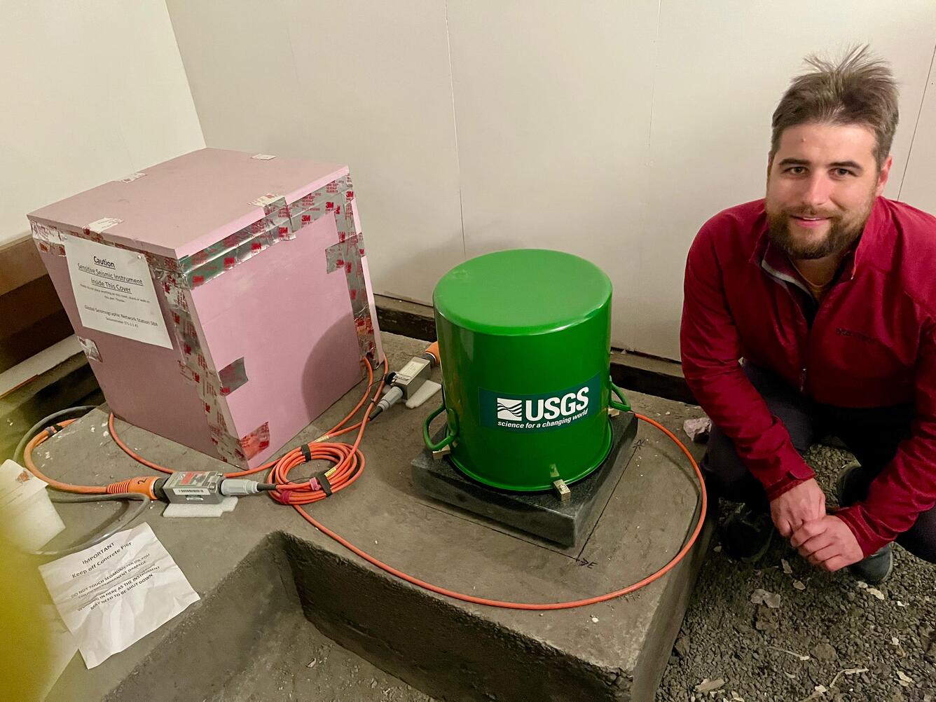 RobAnthony posing next to a seismometer in the South Pole