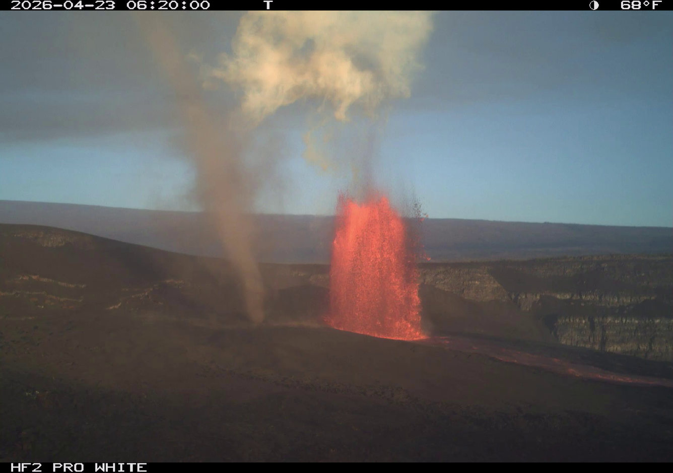Color photograph of lava fountain during daylight with a dust devil nearby