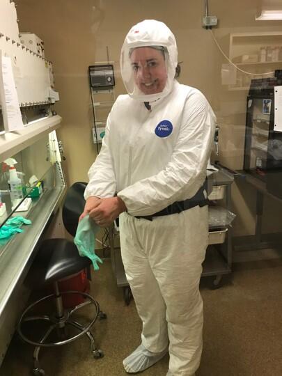 Scientist putting on PPE including respirator, tyvek suit, gloves, and shoe coverings in a laboratory.