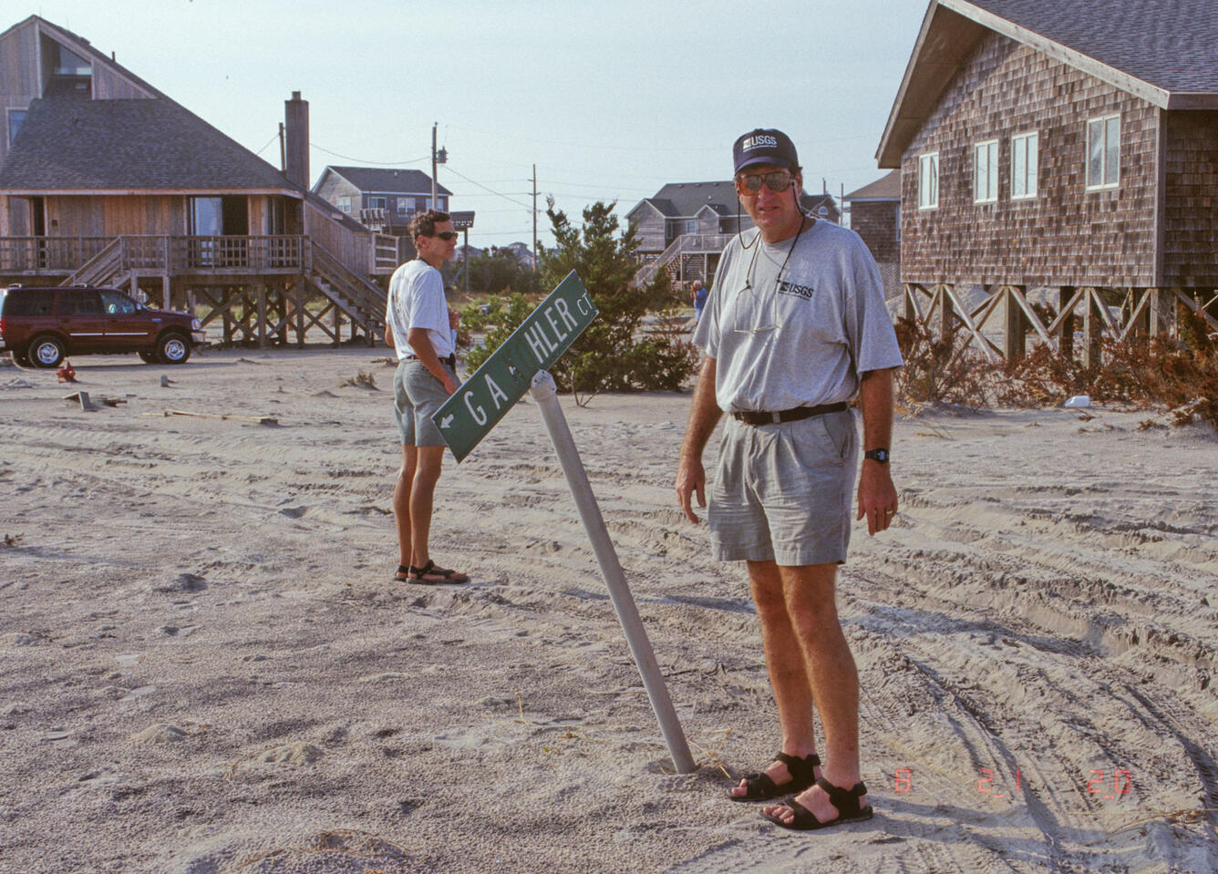 Two men stand by a street sign that is falling over.