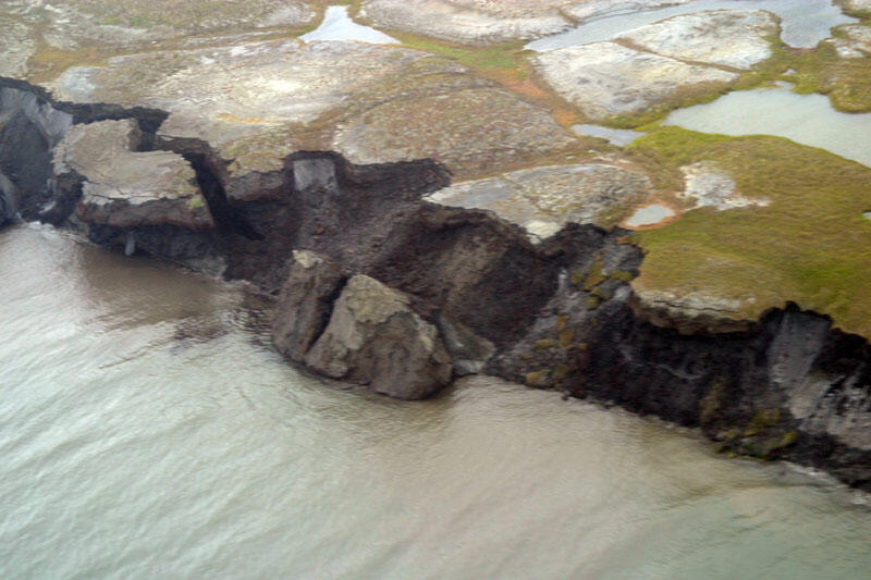 The edge of an island that is crumbling and falling into the ocean water that is calm in the photo.