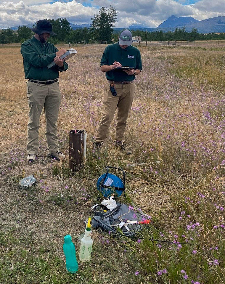 Two hydrologists survey a groundwater well in early summer amongst wildflowers