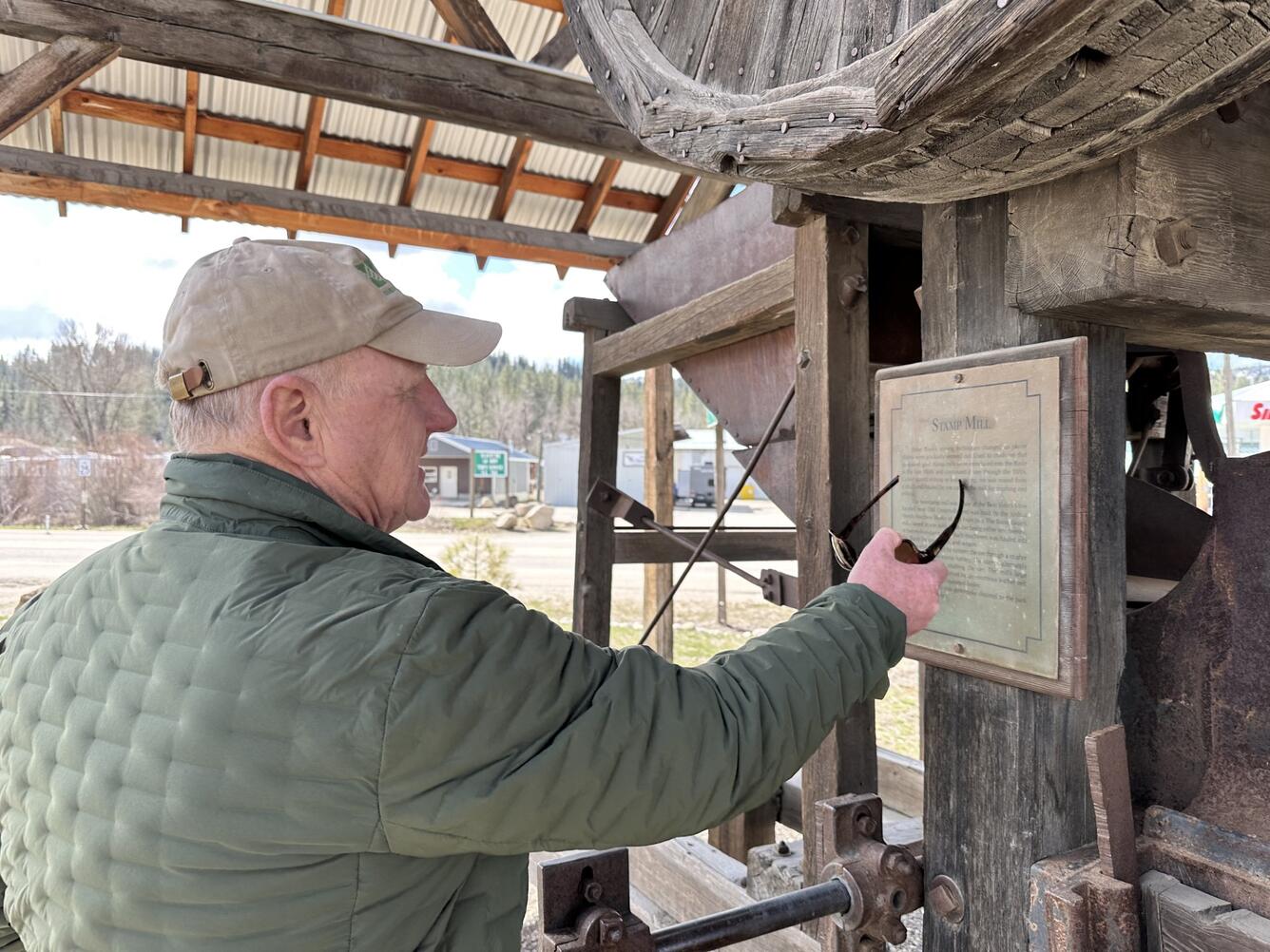 Image shows a man in a baseball cap and coat pointing at old mining machinery
