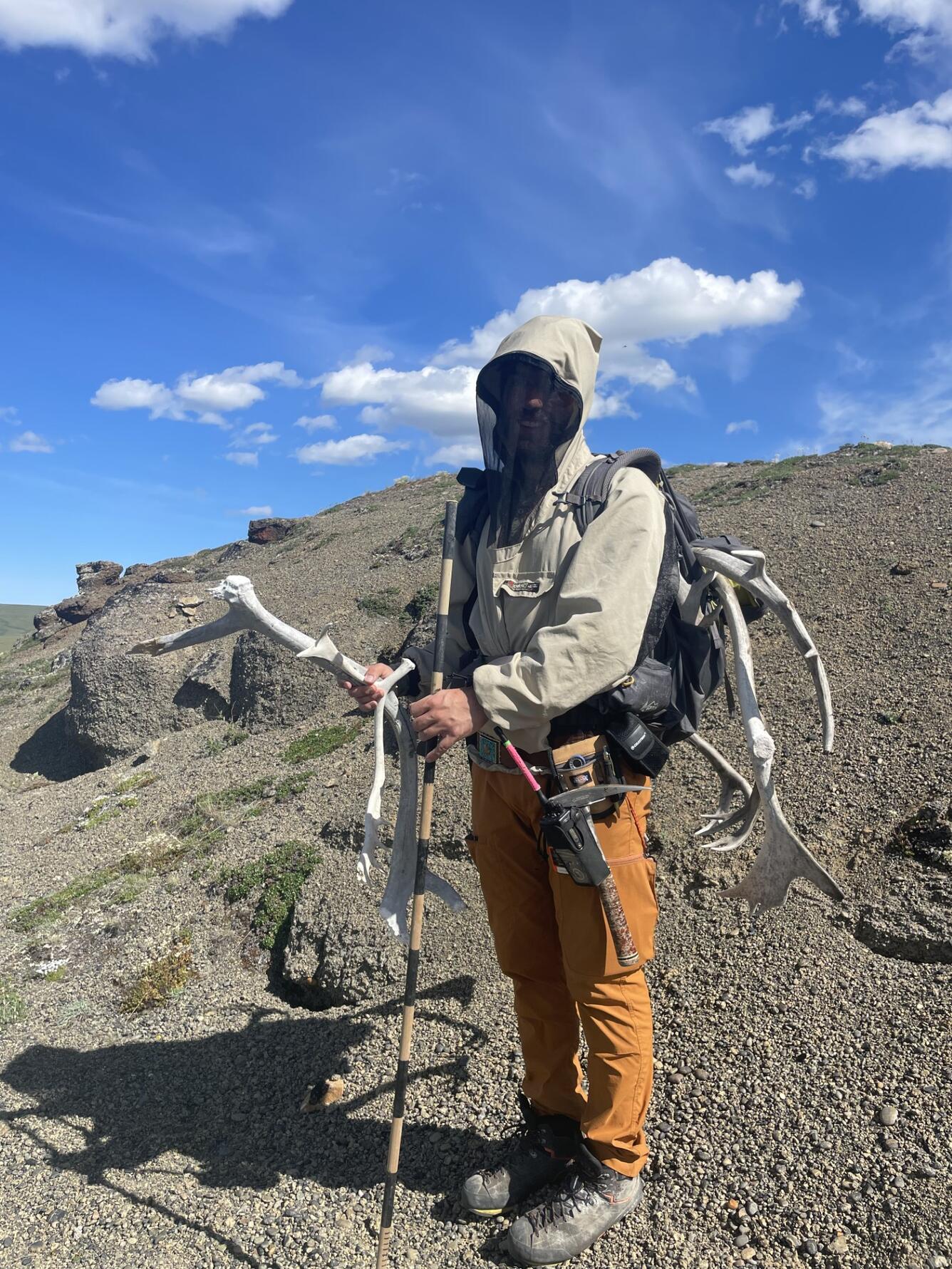 Amit standing on a rocky hill, holding antlers and a measuring stick