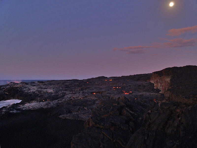 This is a photo of small patches of surface lava in new flow on Banana delta, chaperoned by a nearly full moon.