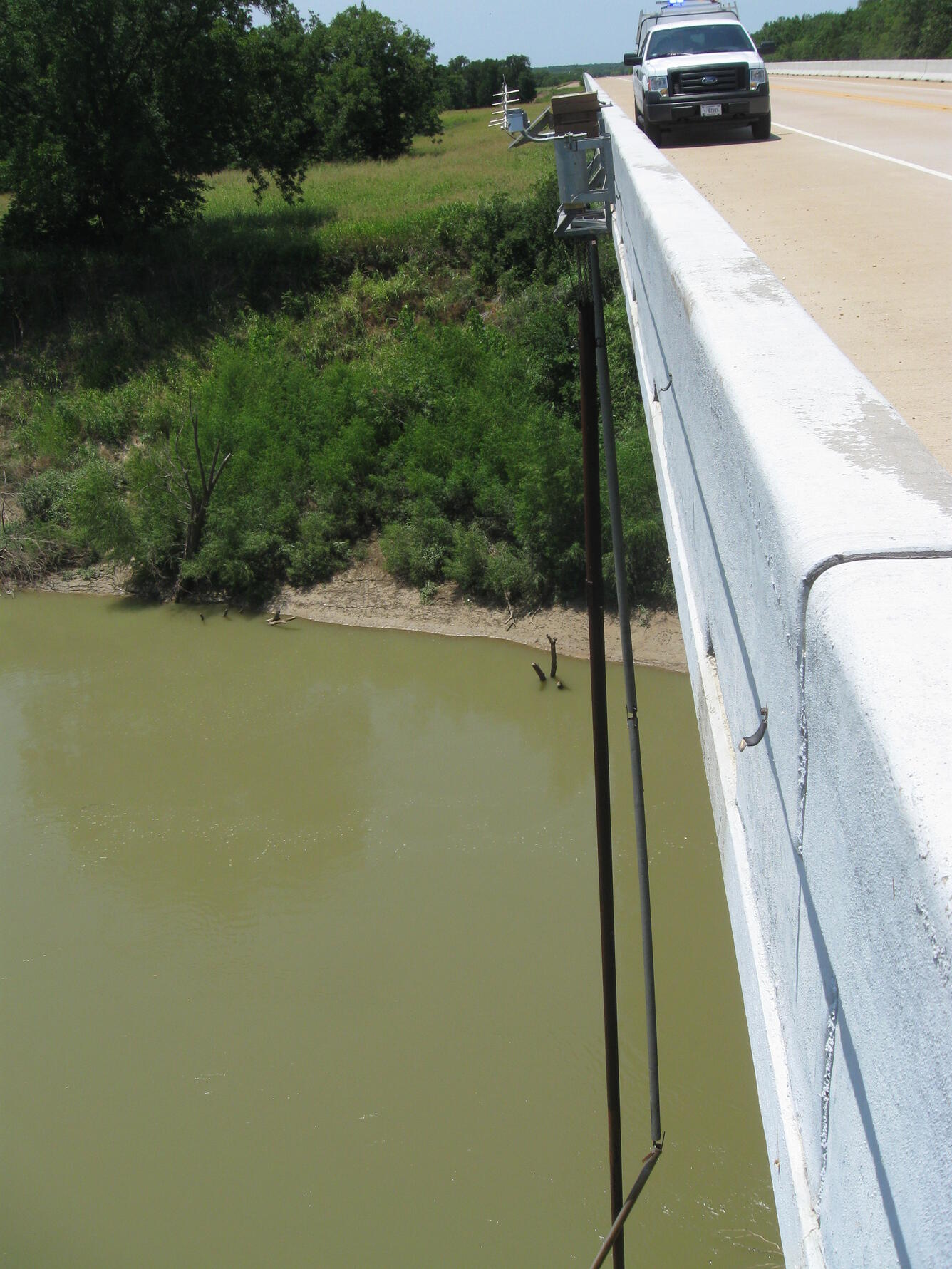 Bridge on right of frame, with orifice line extending down to the river far below.  USGS truck parked on the side of the bridge.