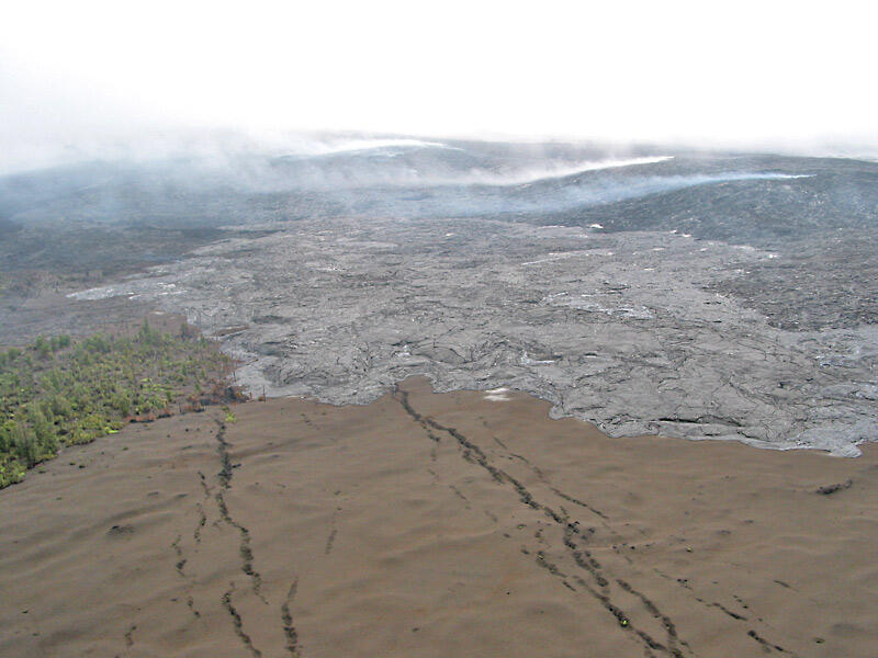 This is a photo of lava flow gradually spreading across brown tephra deposit produced by high fountains from Pu`u `O`o.