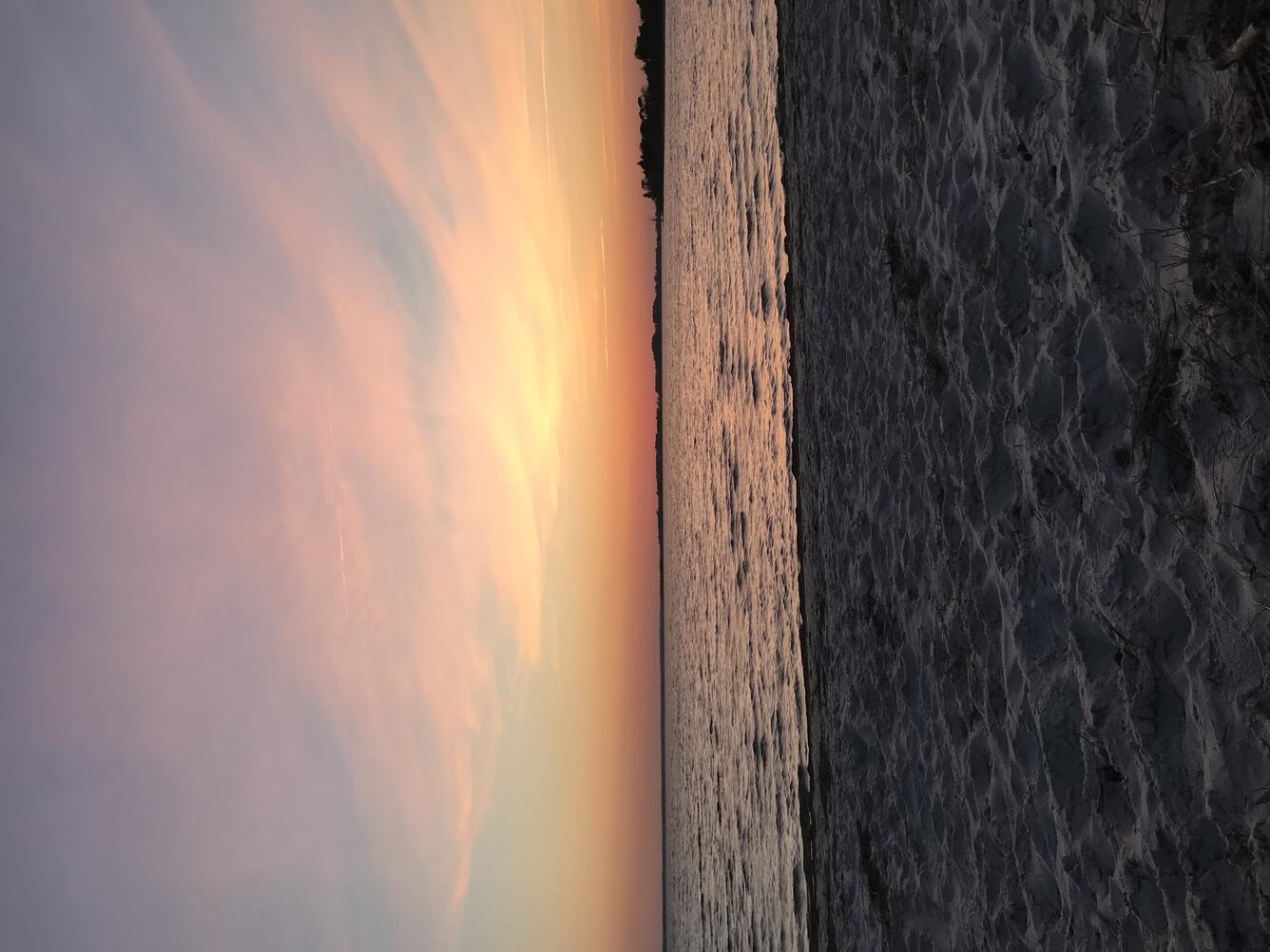 This color photograph shows an orange, pink, and light blue gradient sky at sunset. The colors in the sky are reflected onto the
