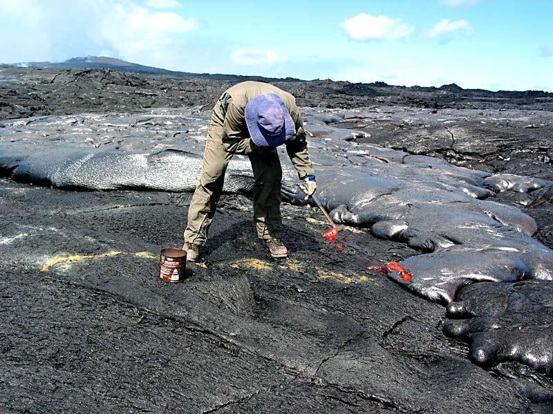 This is a photo of a researcher sampling lava the old-fashioned way, with a rock hammer.